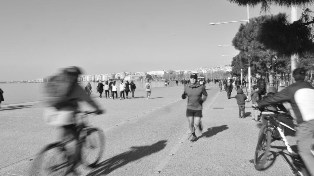 Black and white photo of a busy seaside promenade with cyclists and runners.